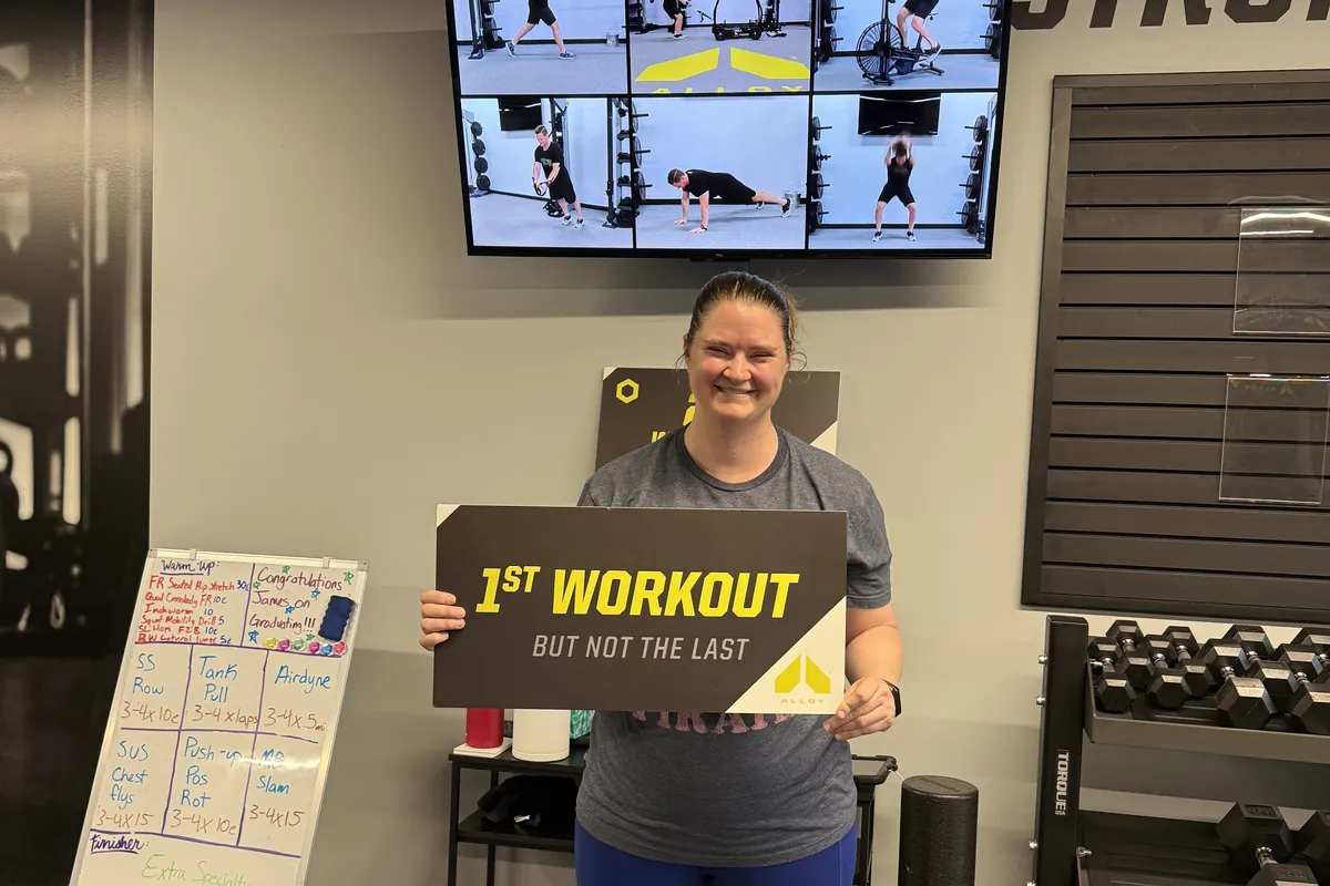 Member holding a first-workout milestone sign at Alloy Personal Training Fairfax City
