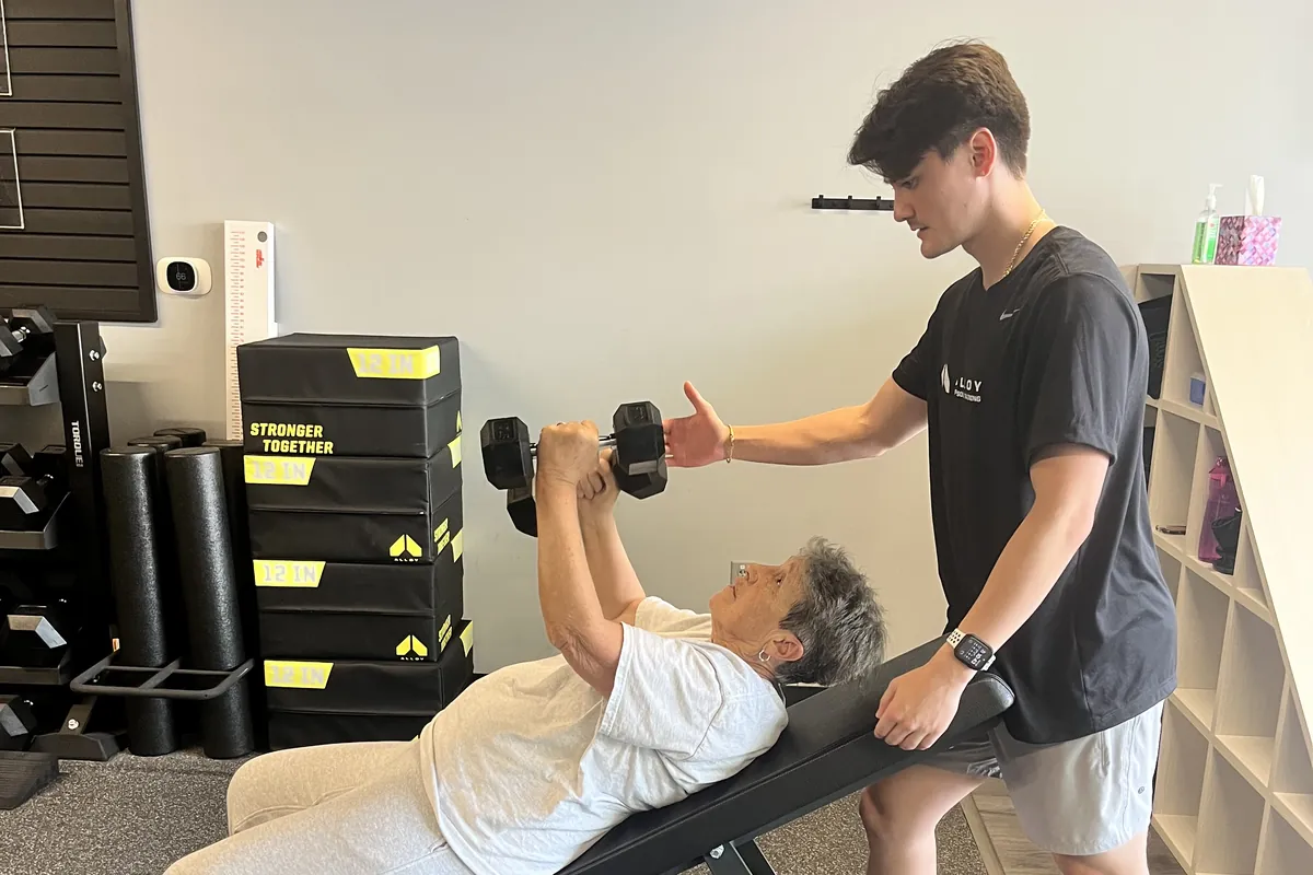 Coach guiding a member through a dumbbell press at Alloy Personal Training Fairfax City